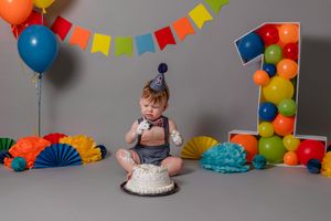 cake smash session, grey background with rainbow colored balloons and decorations