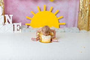 you are my sunshine cake smash session. toddler girl wearing yellow dress diving head first into cake