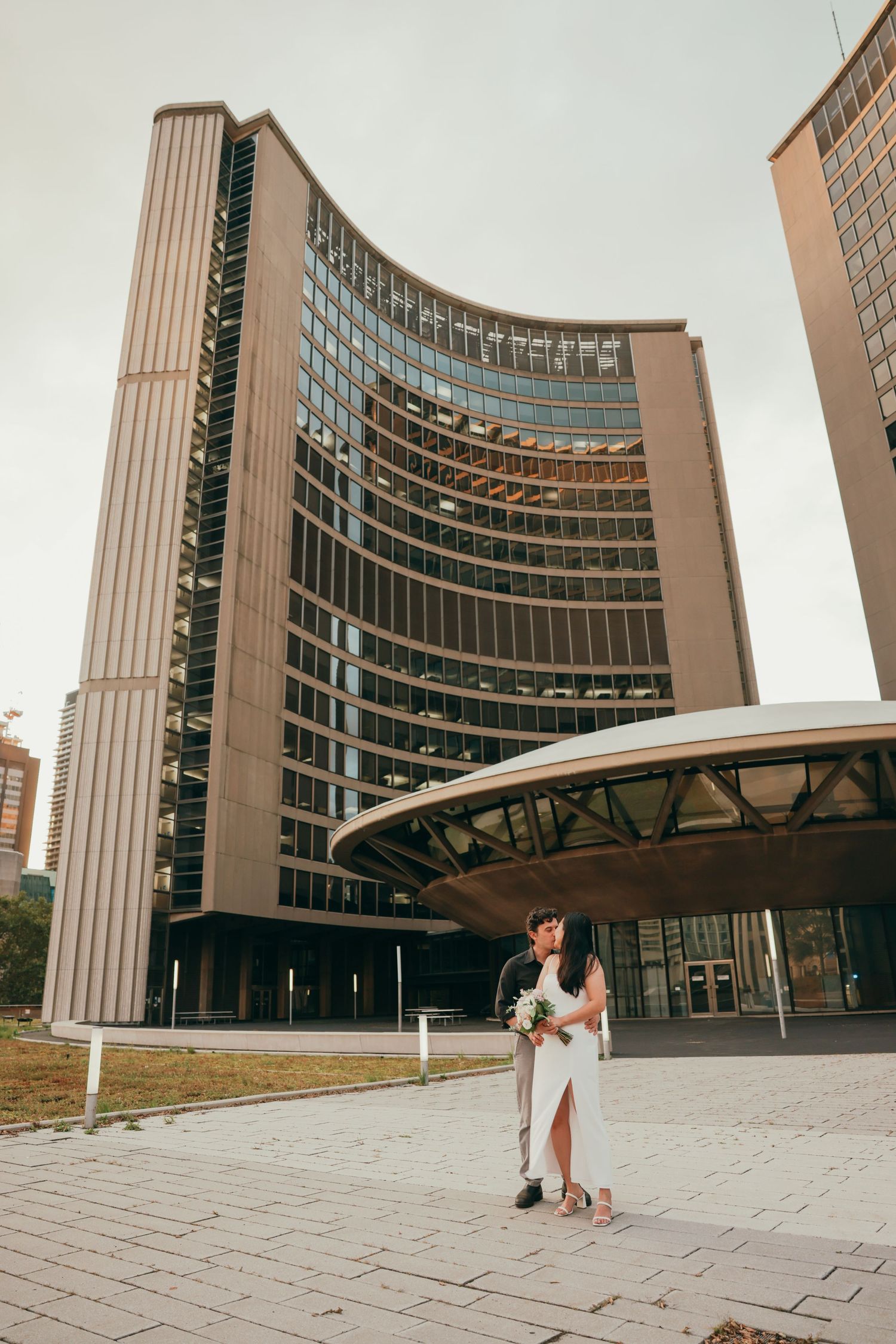 A couple poses outside Toronto City Hall with its distinctive curved architecture.