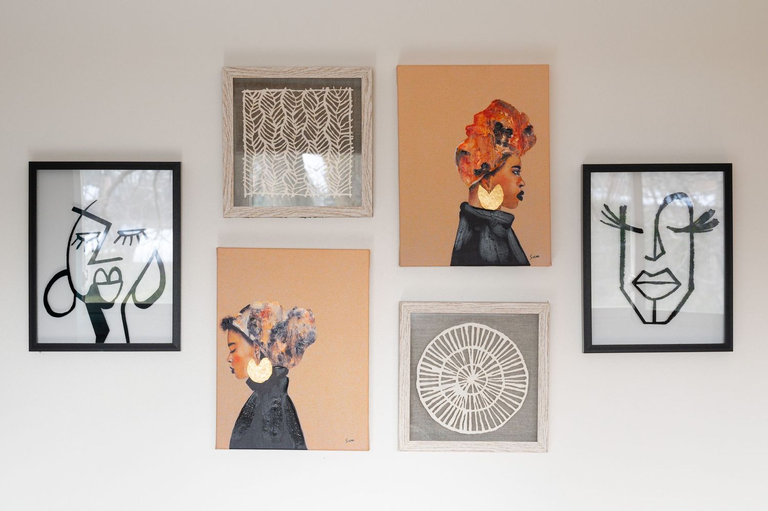 A gallery wall display featuring abstract black and white line drawings and orange-toned artwork arranged in a grid pattern.