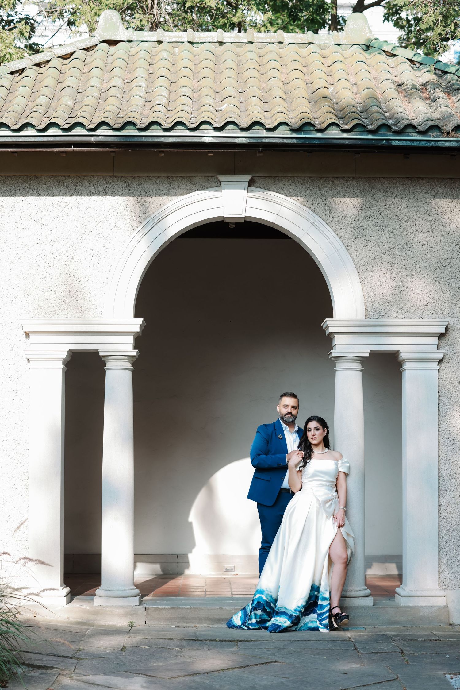 A couple stands under an arched colonnade with Mediterranean-style tile roof.