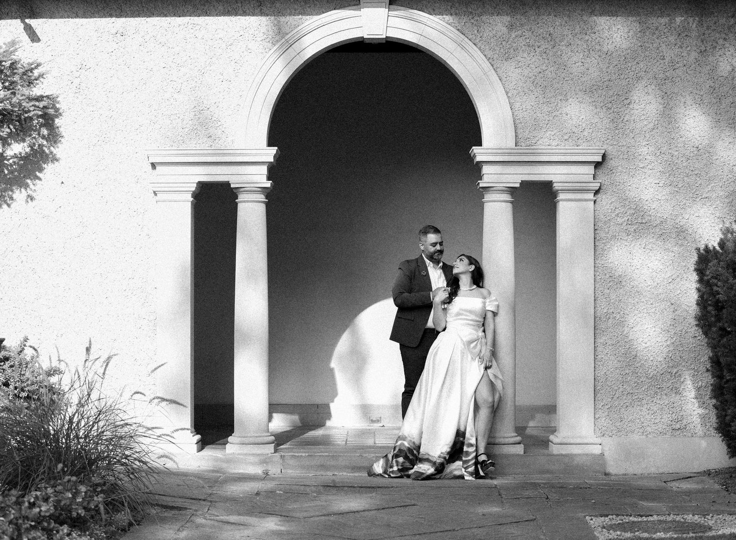 Black and white wedding photo under classic archway with flowing dress details.