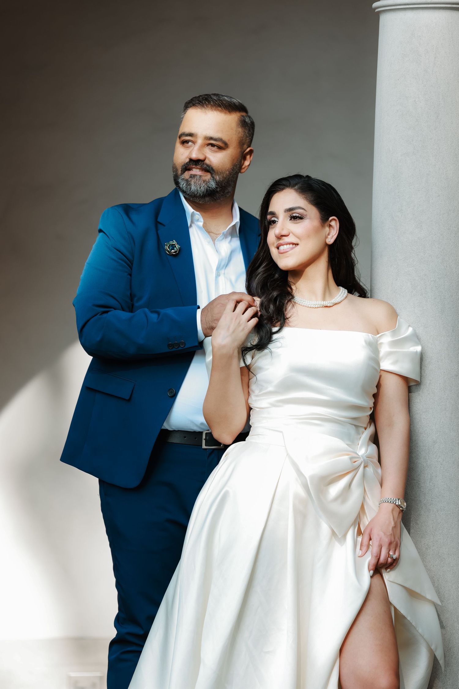 Stylish wedding portrait with couple posed against architectural column in dramatic lighting.