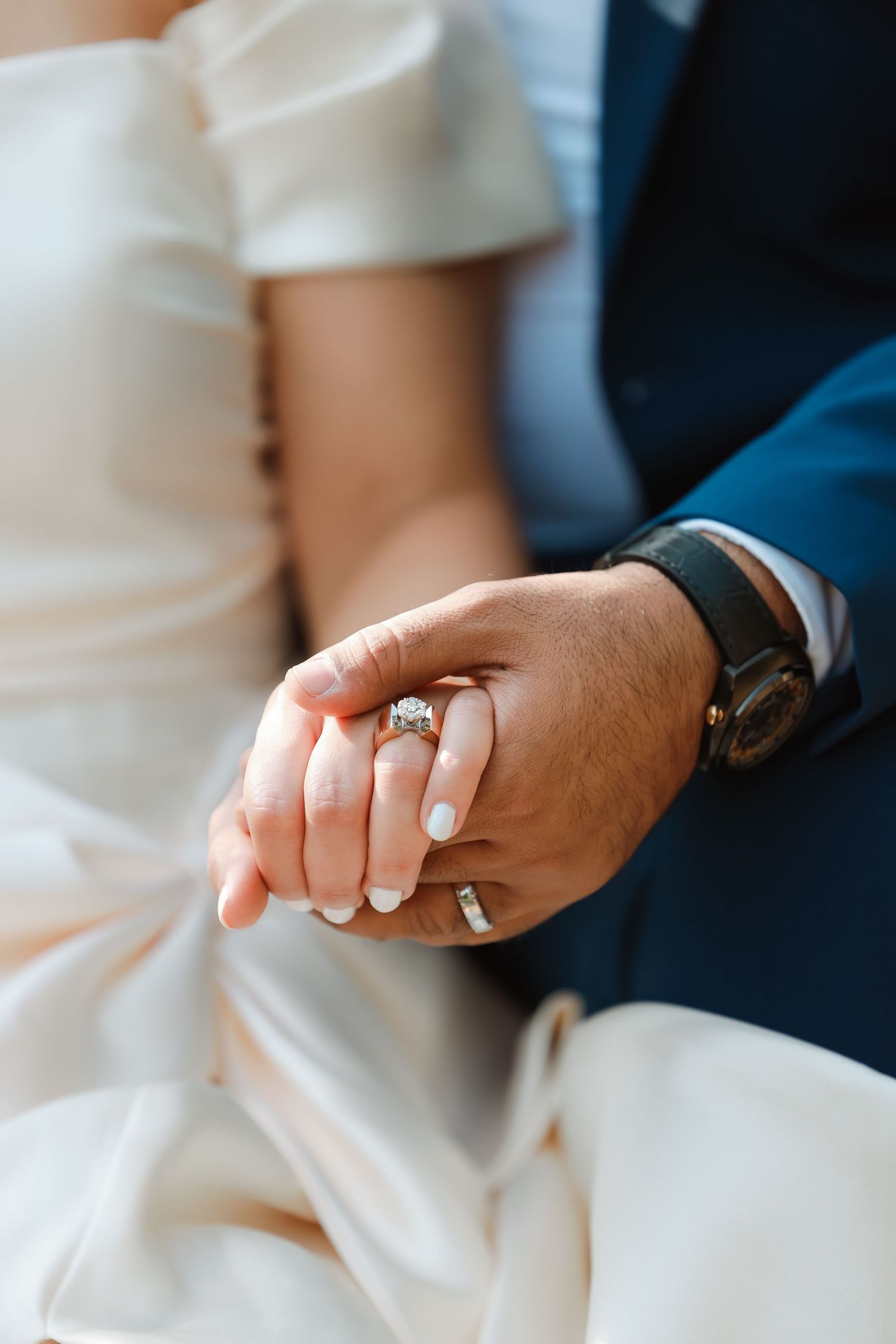 Close-up of hands with wedding rings against white dress fabric.