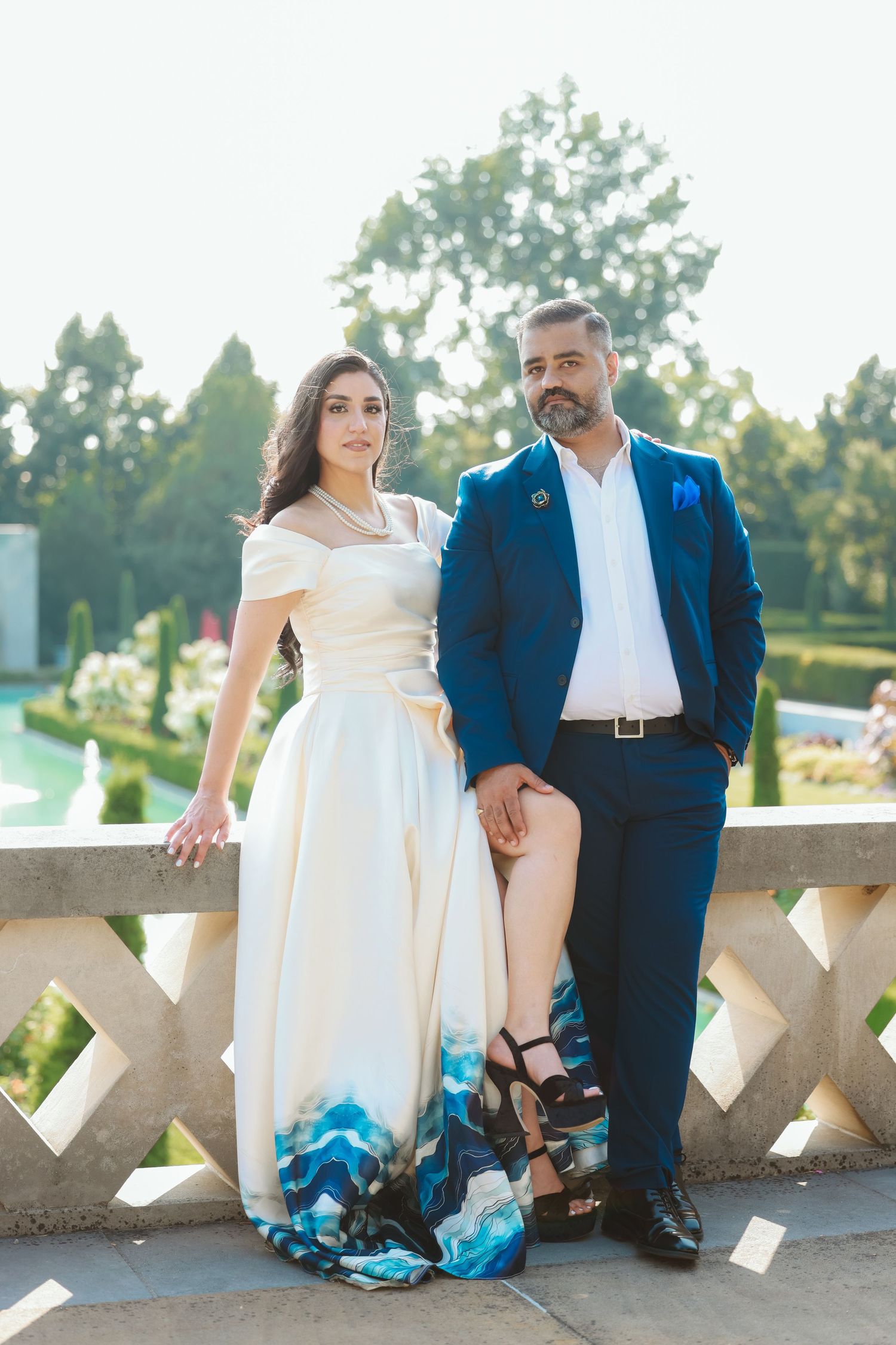 Couple in formal attire standing against stone railing, dress featuring blue ombre details.