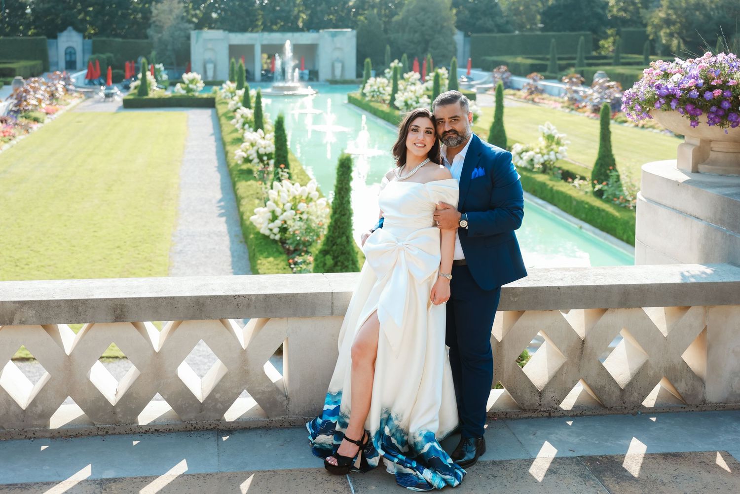 Elegant garden wedding portrait with couple standing on terrace above reflecting pool and formal landscaping.