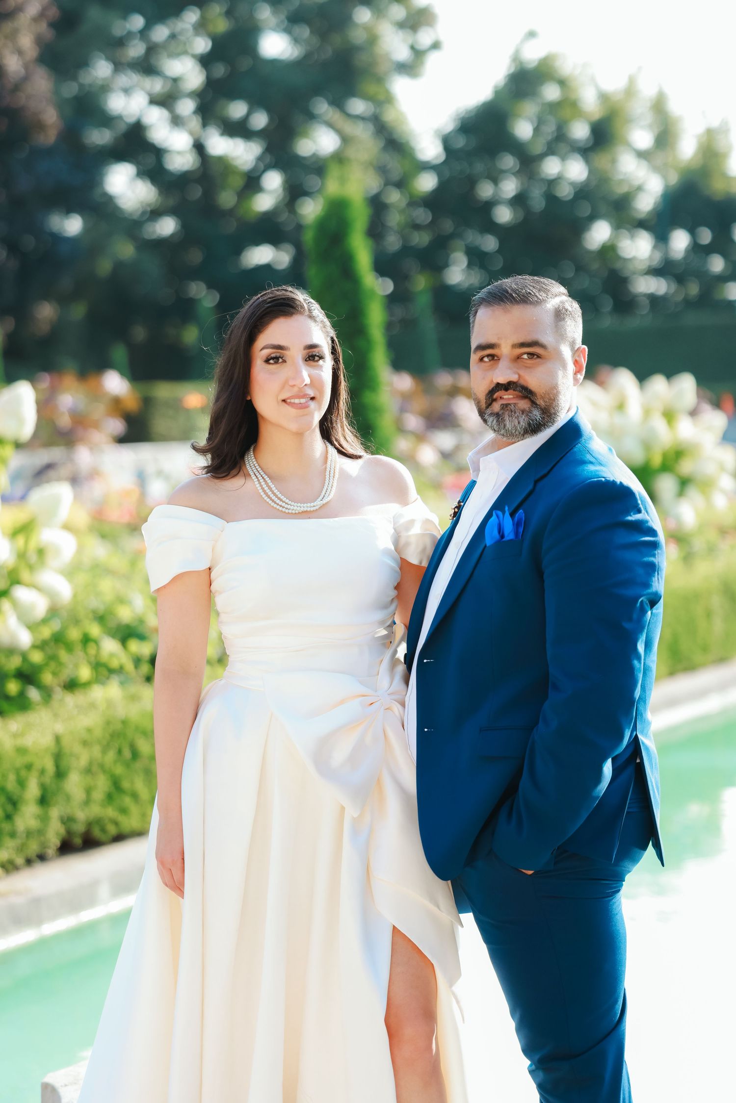 Formal wedding portrait in elegant garden setting with reflecting pool and flowering landscaping.