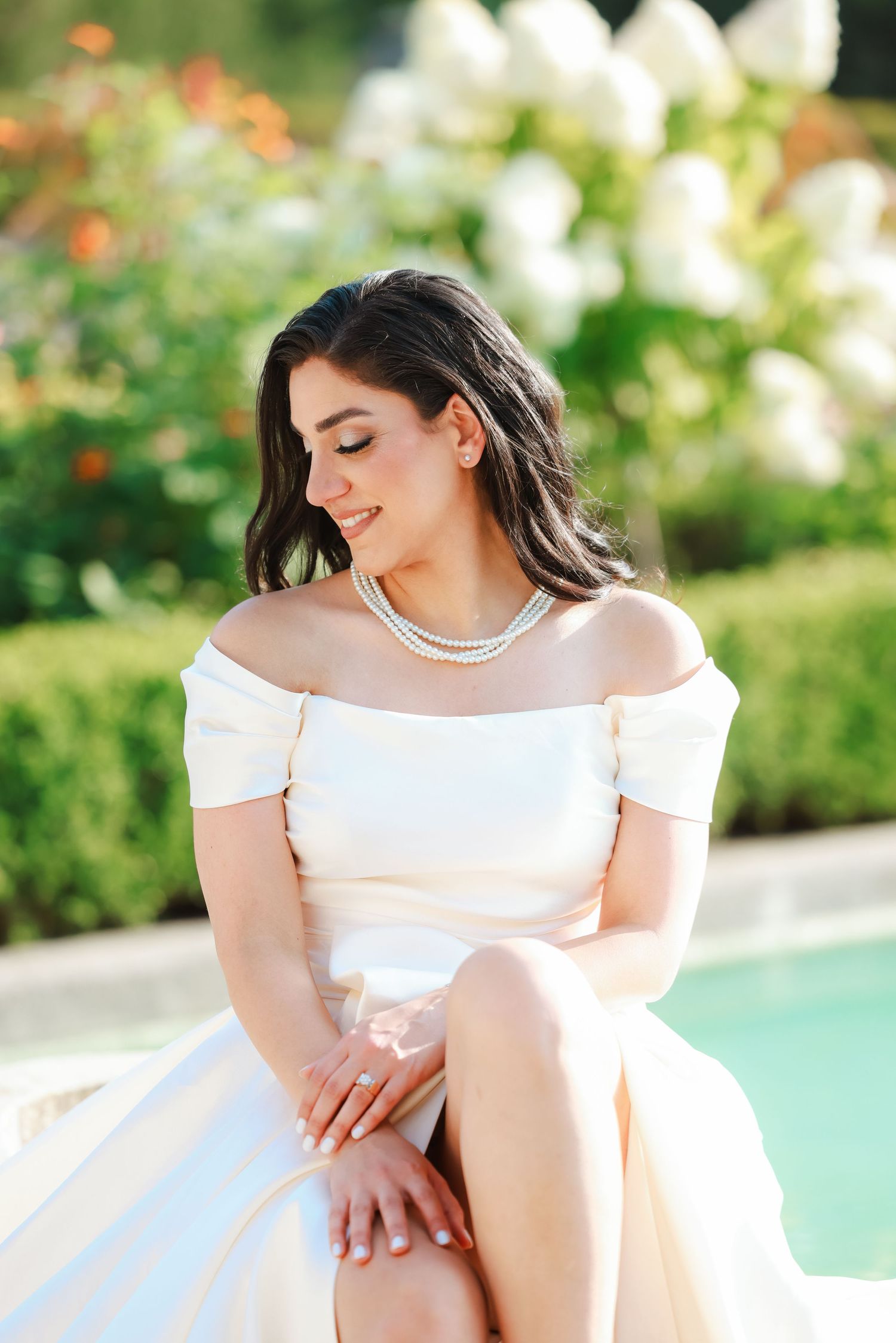 Off-shoulder white dress and silver necklace photographed in a sunny garden setting.