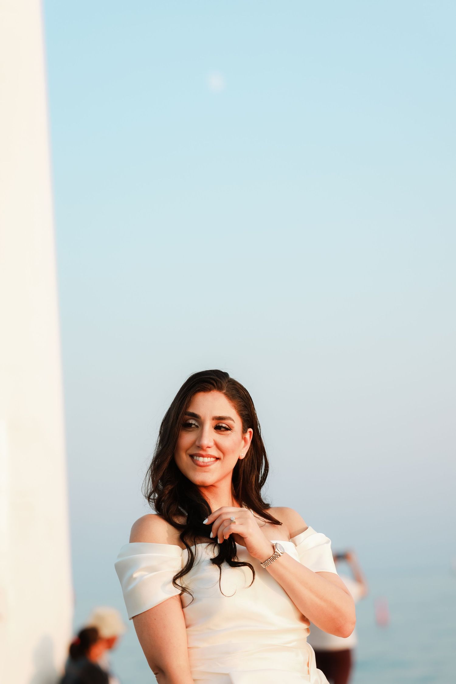 A bride in white poses against a soft blue sky background at golden hour.
