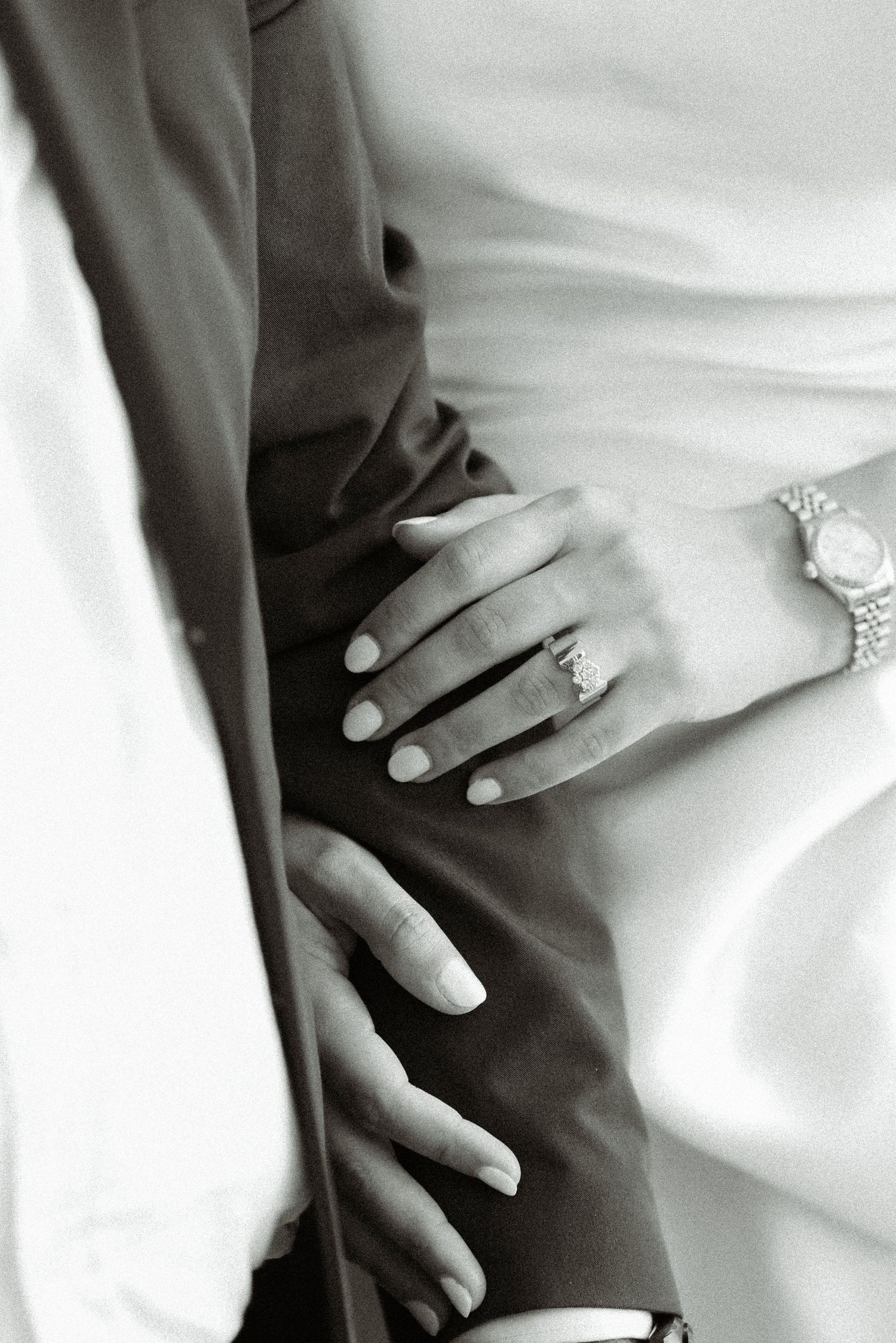 Close-up black and white photo of hands with wedding rings against formal attire.
