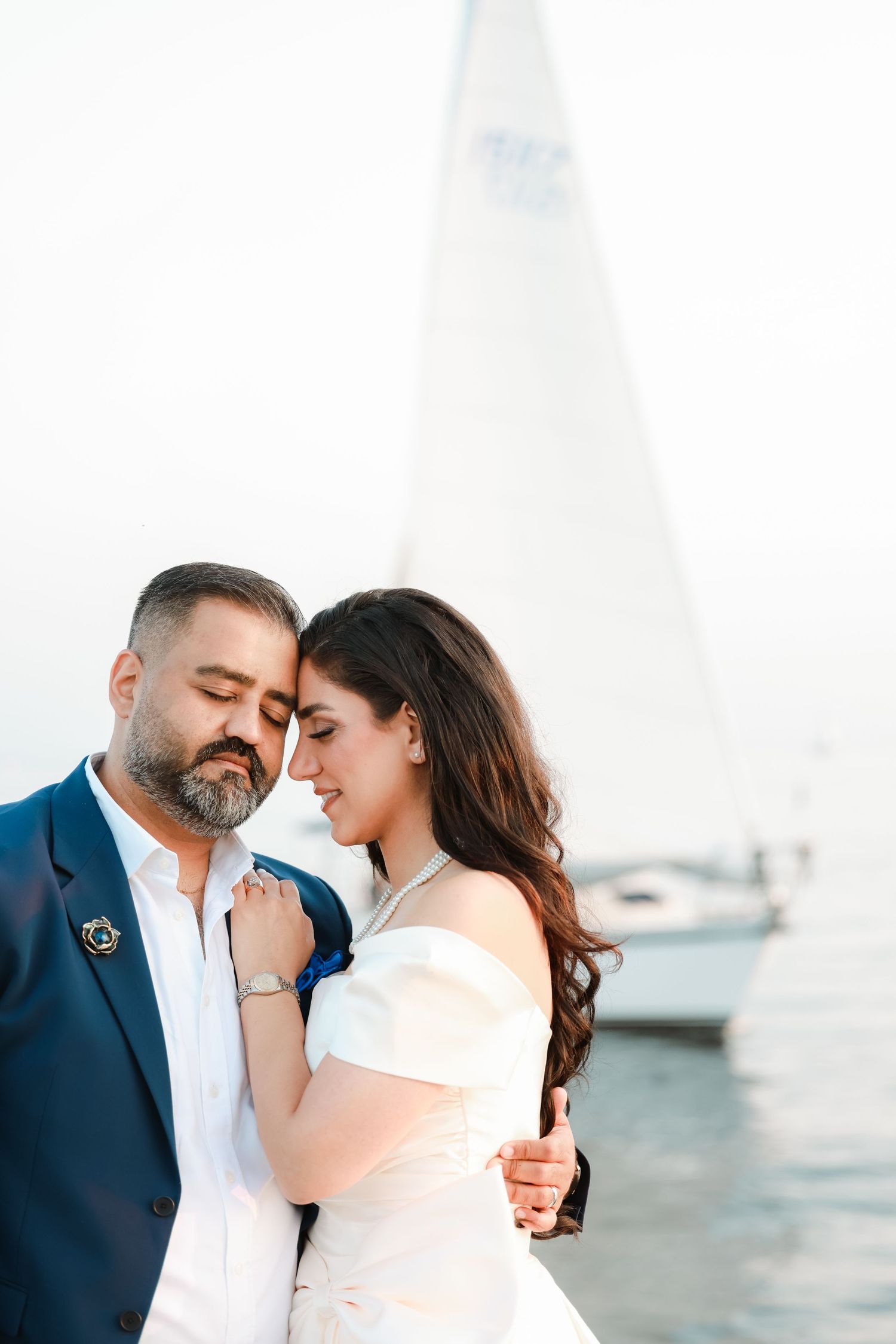 Intimate seaside wedding portrait with couple sharing a romantic moment near a sailboat.