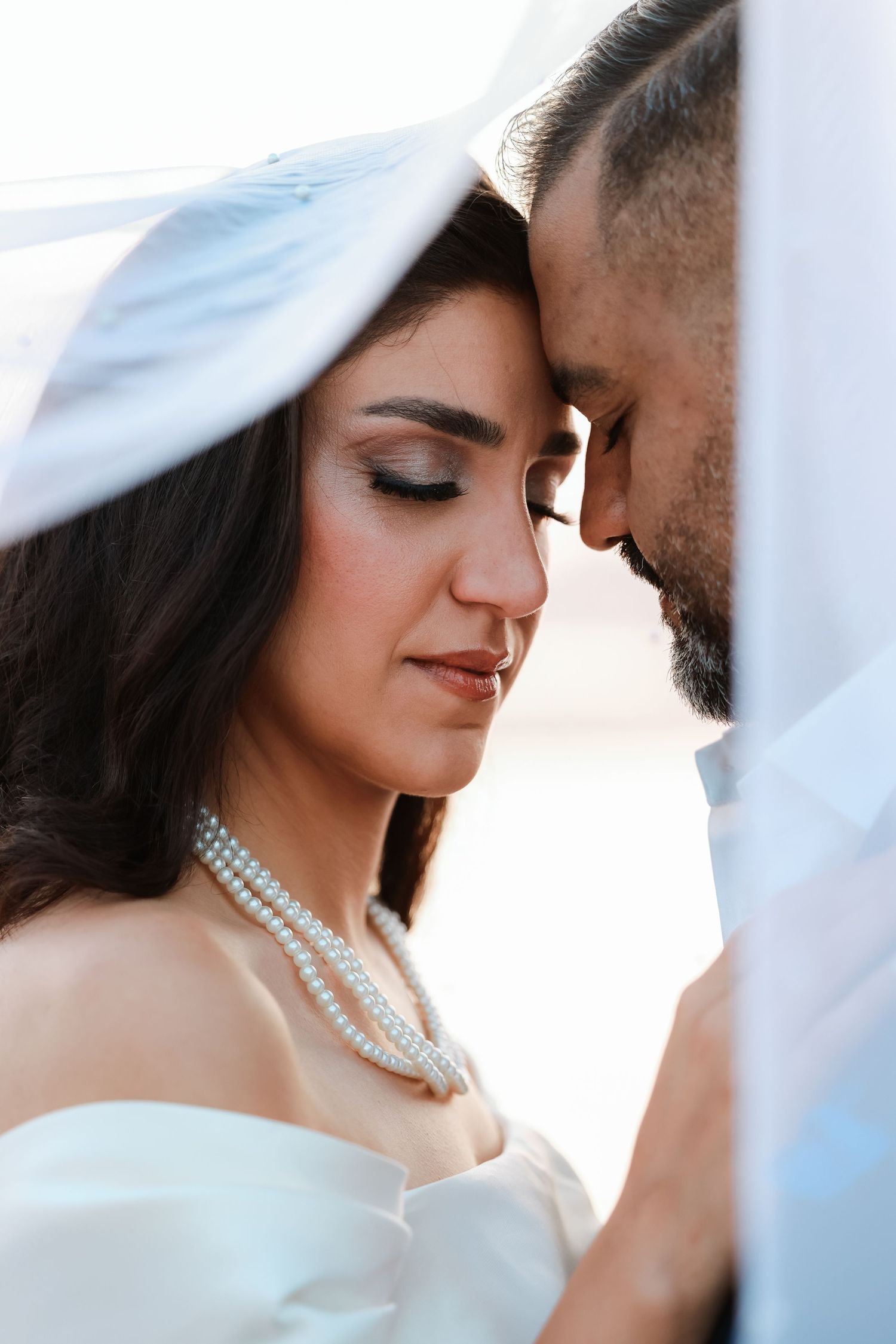 Intimate wedding portrait with pearl necklace detail and soft natural lighting.