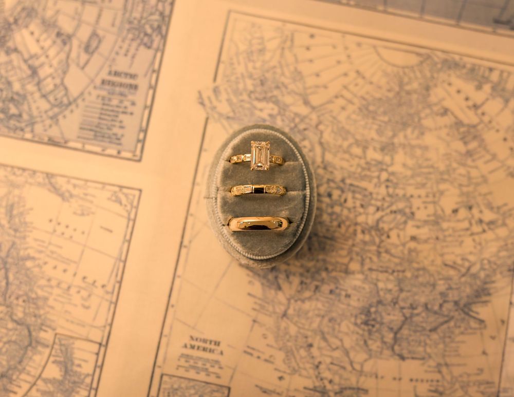 Three gold rings displayed on an oval gray velvet ring holder resting on top of vintage antique world maps.