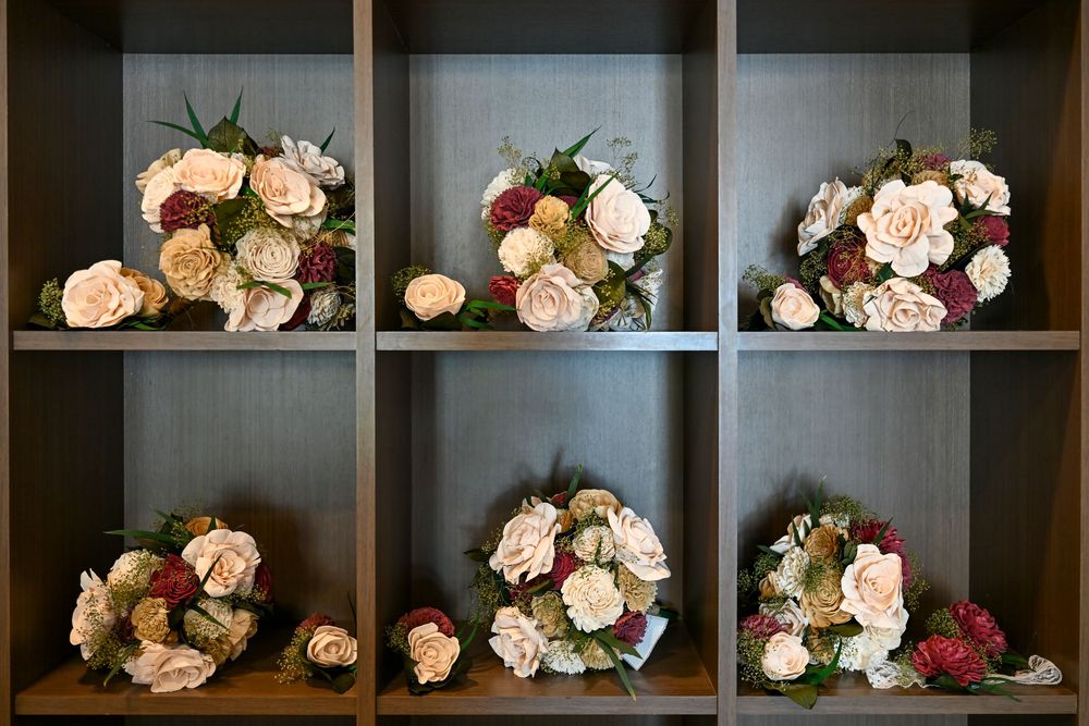 Six bridal bouquets of cream, blush and burgundy roses displayed on dark wooden shelves in a floral shop or wedding venue.