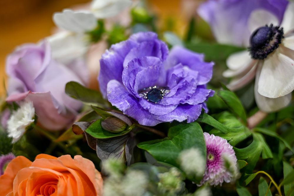 Wedding ring with blue stone nestled inside purple anemone flower in bridal bouquet.