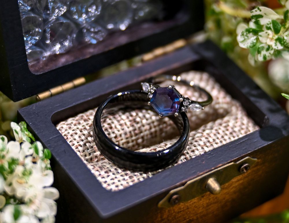 Black wedding ring set with blue sapphire displayed in wooden jewelry box.
