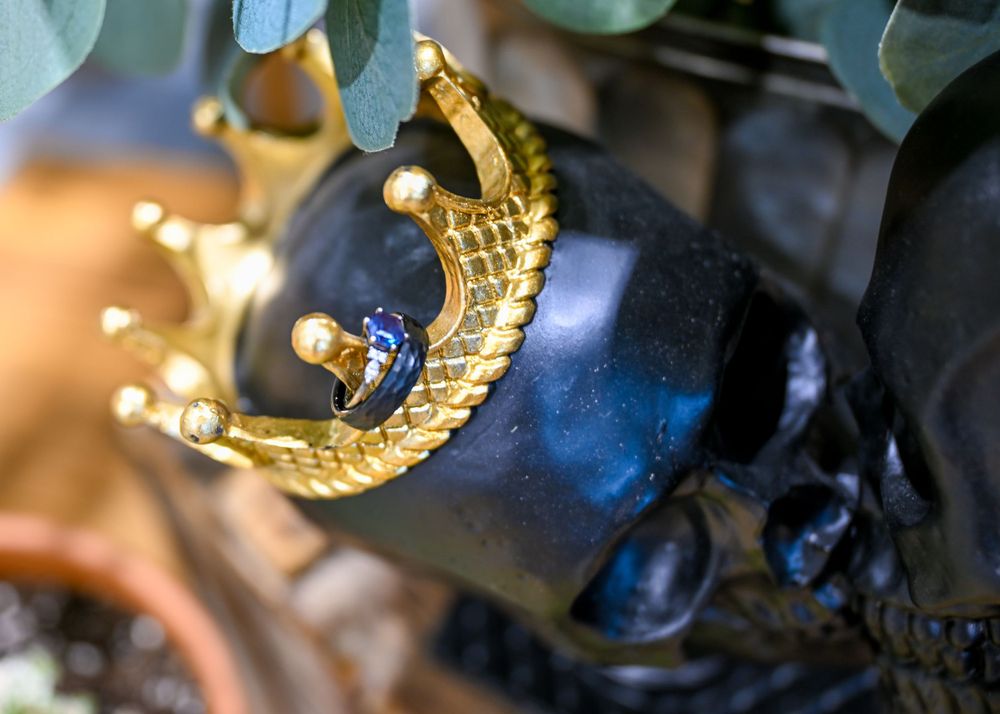 Gold crown ring with blue gemstone resting on black decorative skull with eucalyptus leaves.