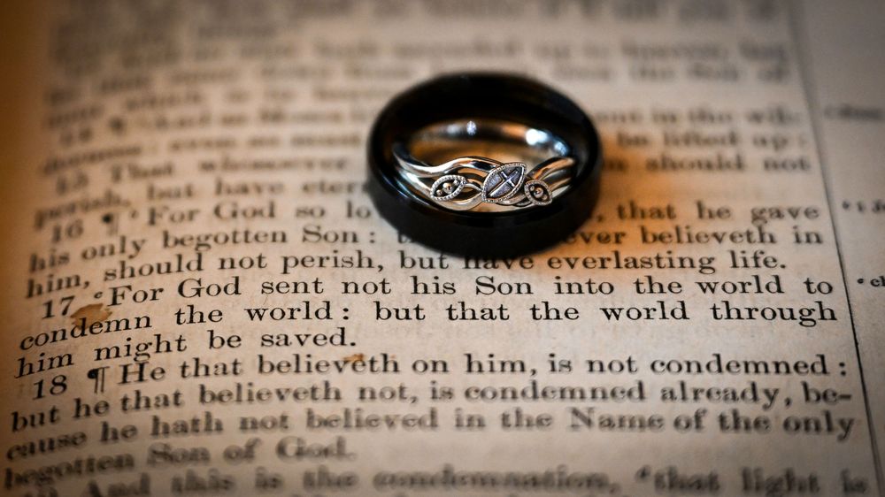 Wedding band resting on an open Bible displaying John 3:16 scripture verse.