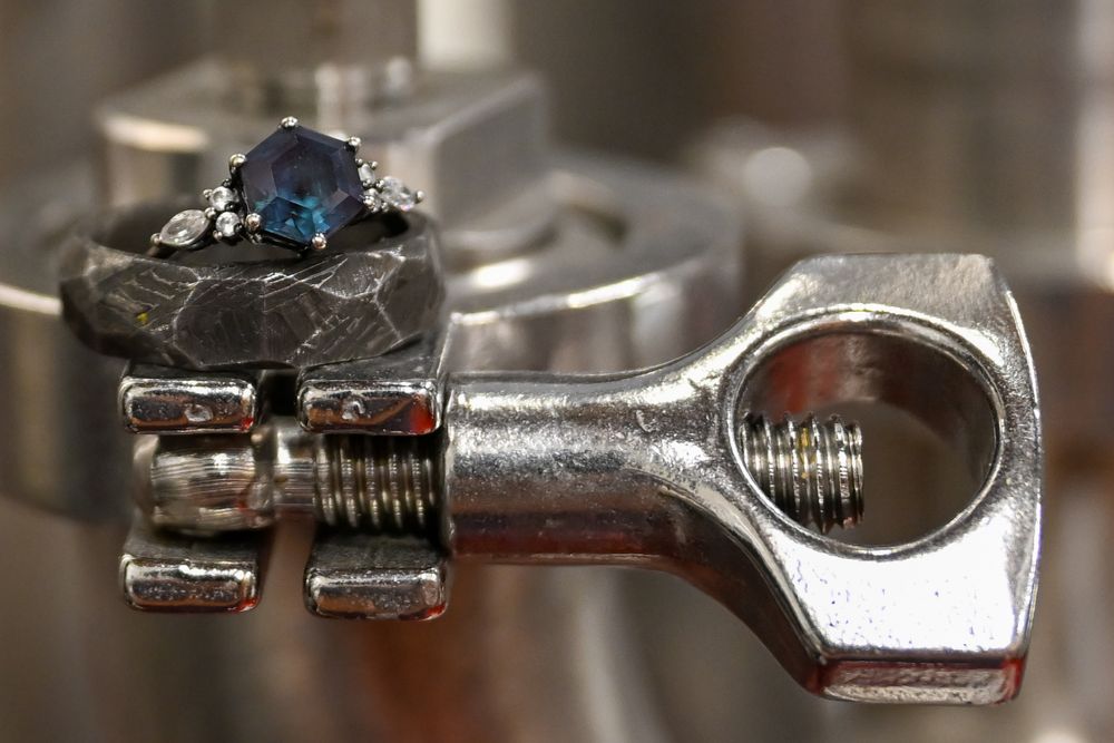 Blue sapphire engagement ring displayed on a silver mechanical engine component.