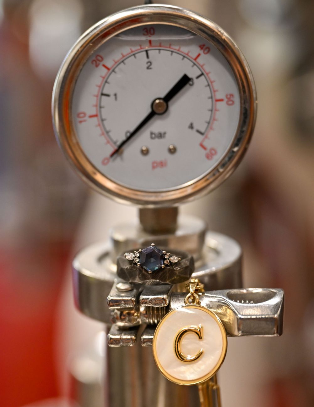 Blue sapphire engagement ring displayed near a pressure gauge on brewery equipment.