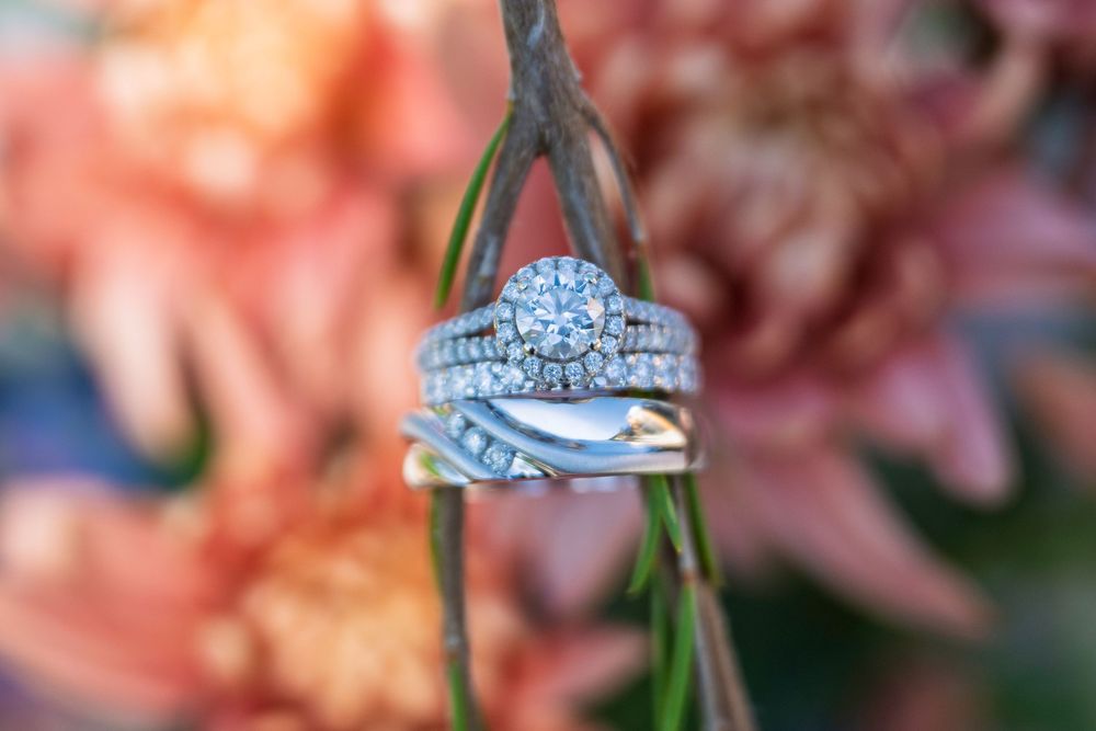 Sparkling diamond halo wedding ring set stacked on a green stem with soft pink floral background.