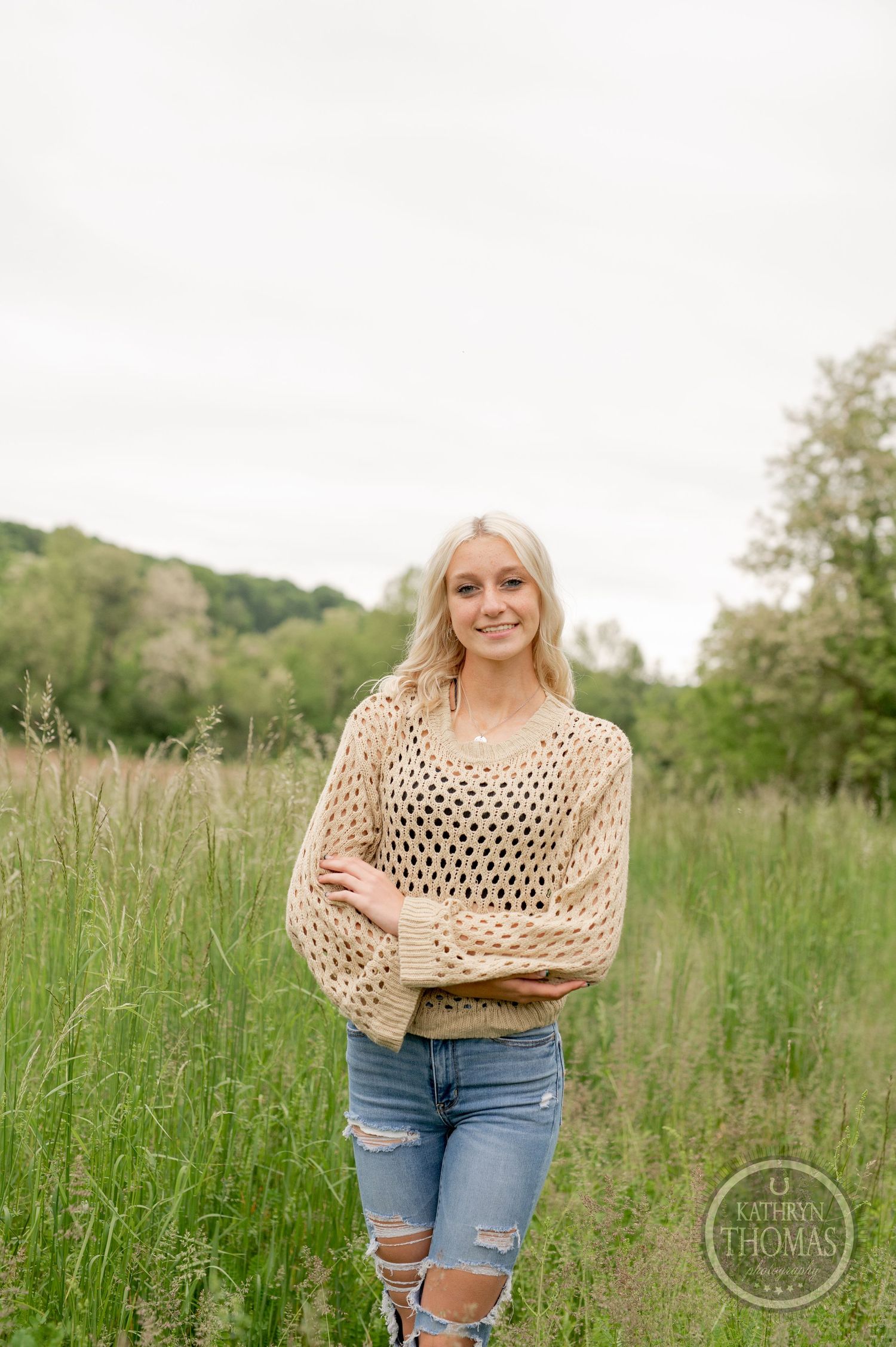 Spring fashion photo in tall grass wearing cream crochet sweater and ripped jeans.