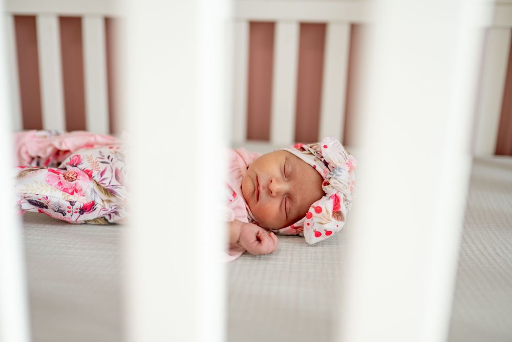 A series of connected photos showing a sleeping newborn baby wearing pink floral clothing against white bedding.