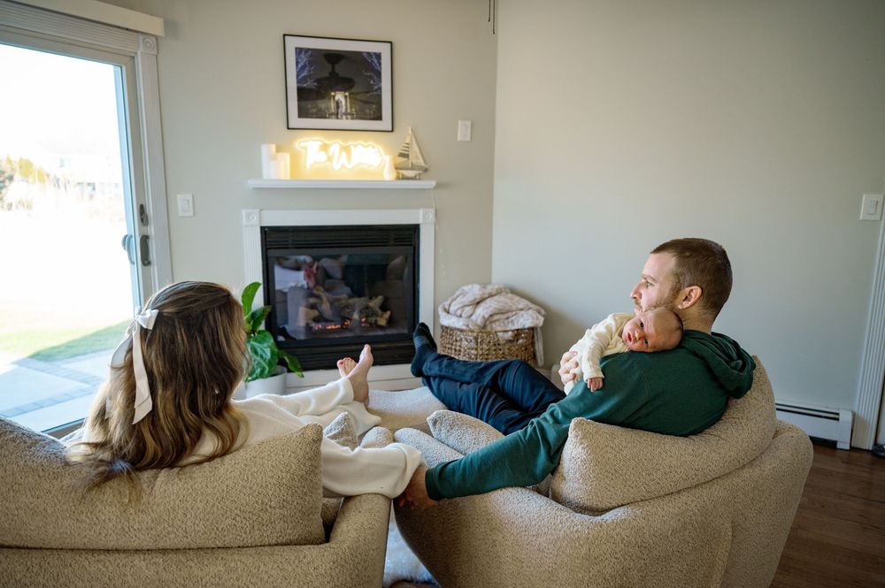 Someone relaxes on a beige couch in a bright living room with natural light coming through the windows.