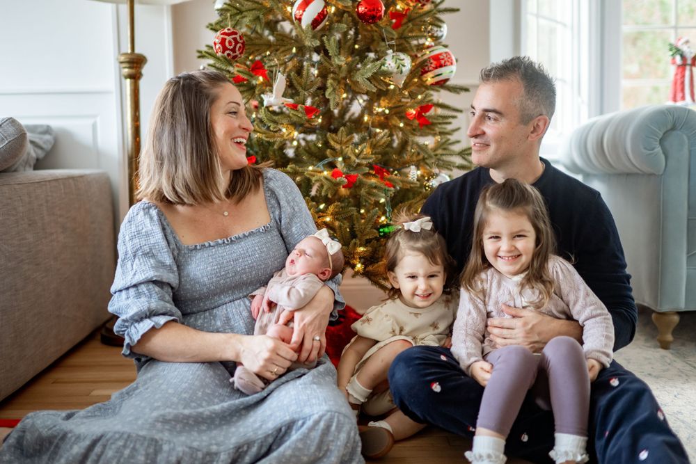A family shares a joyful moment together sitting by their Christmas tree decorated with red ornaments.