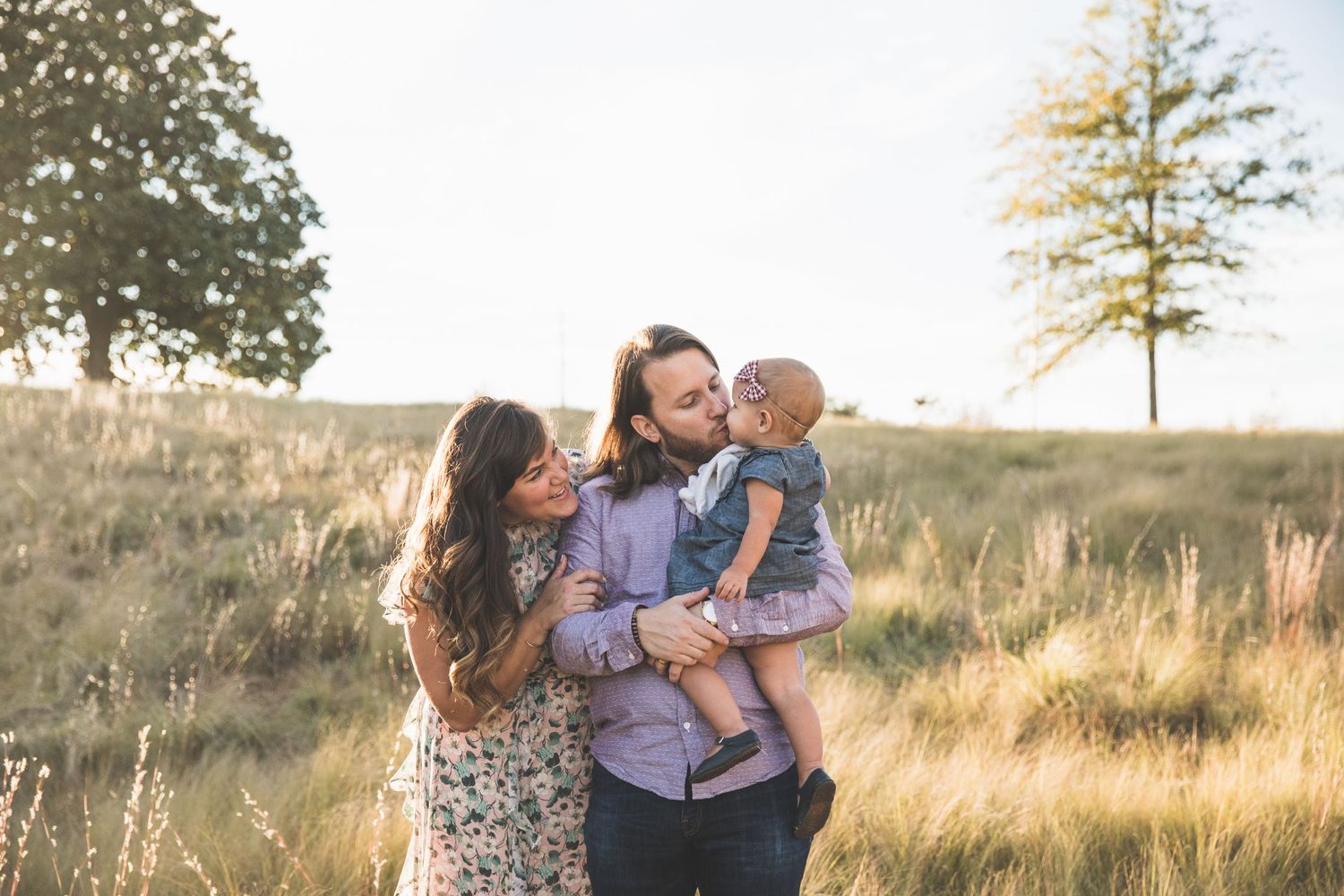 A joyful family moment captured during golden hour in a scenic field with a lone tree in background.