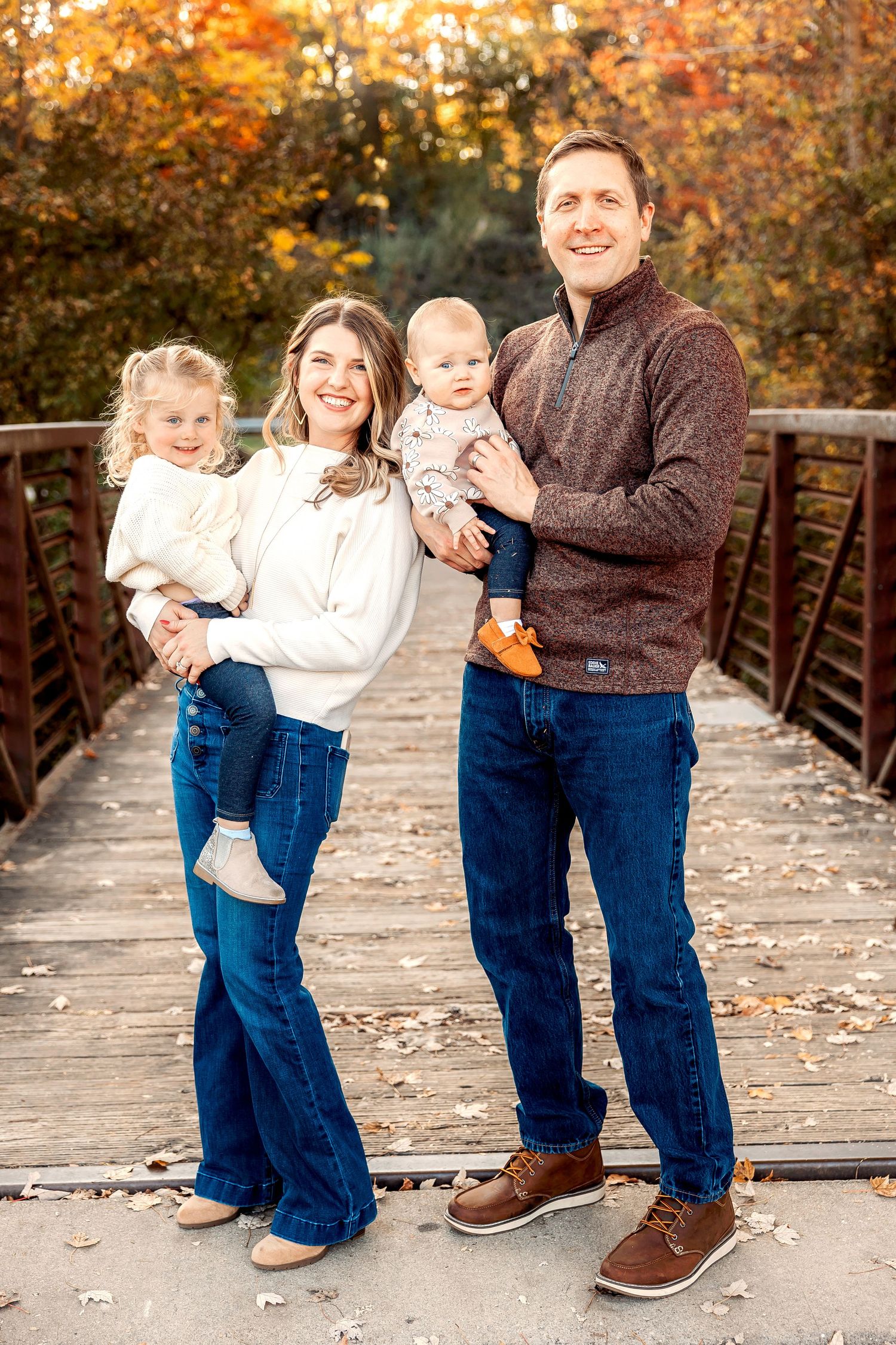 A family stands together on a wooden bridge surrounded by vibrant fall colors. Michigan Detroit Novi Northville Portrait Photographer