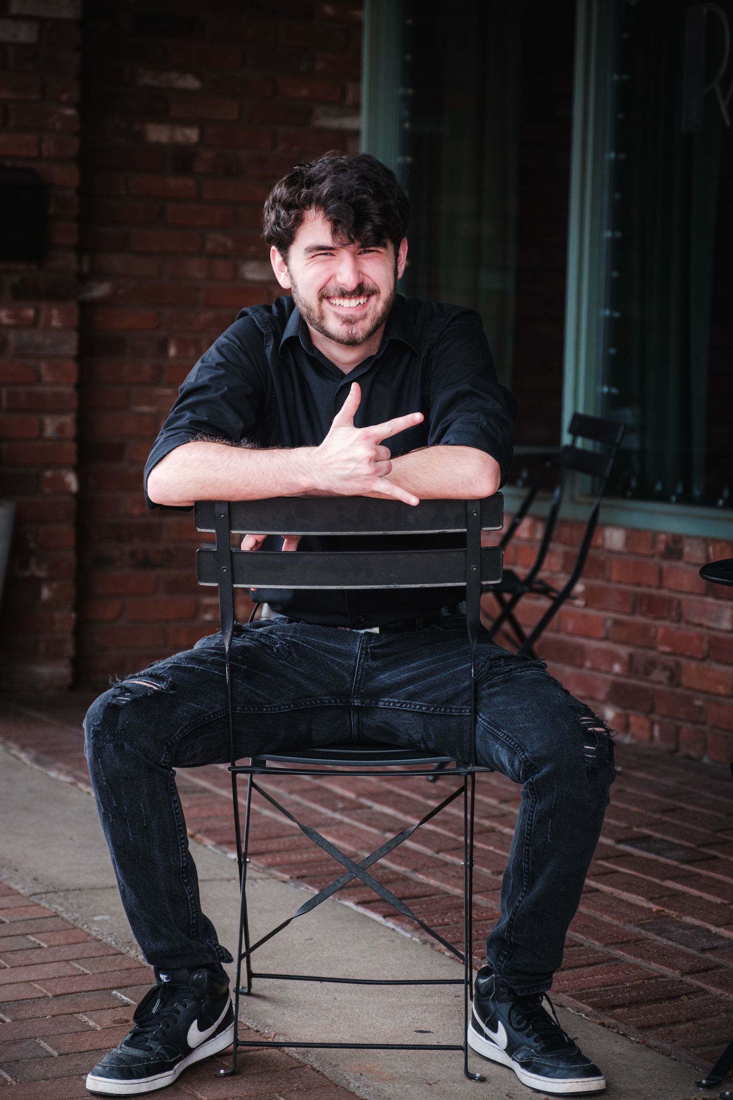 Portrait of a young person in white shirt sitting on wooden stool against urban wall.