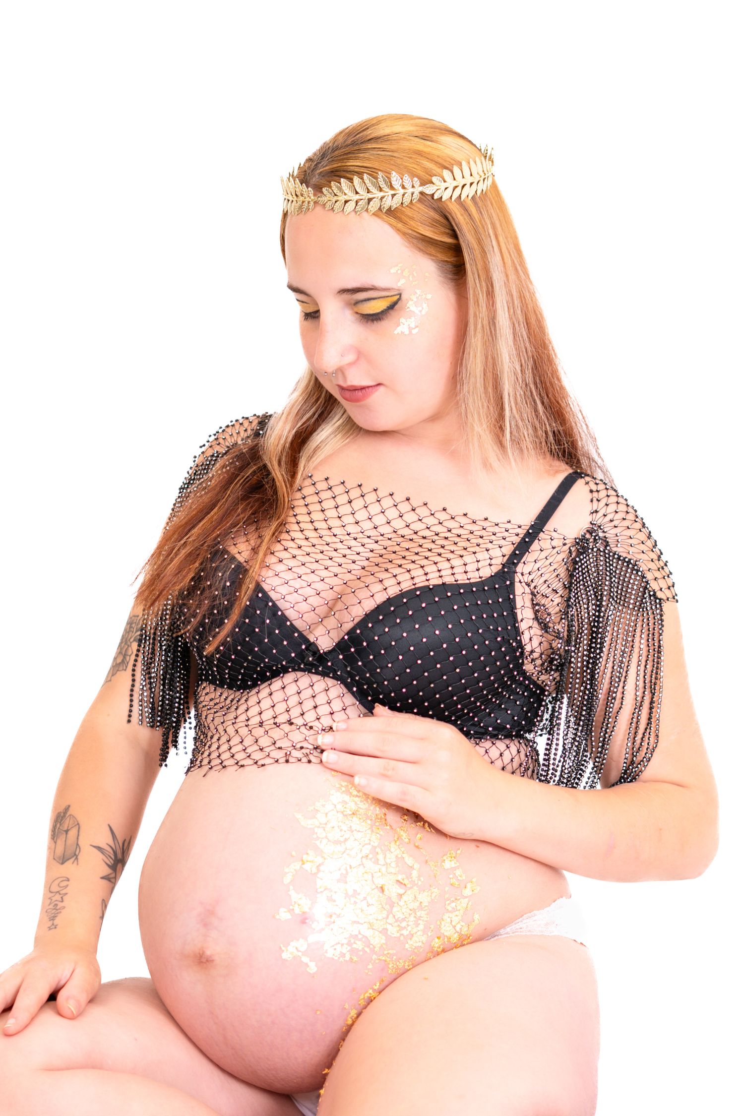 Artistic maternity photo featuring sparkly gold belly art and black lingerie with fringe mesh overlay.