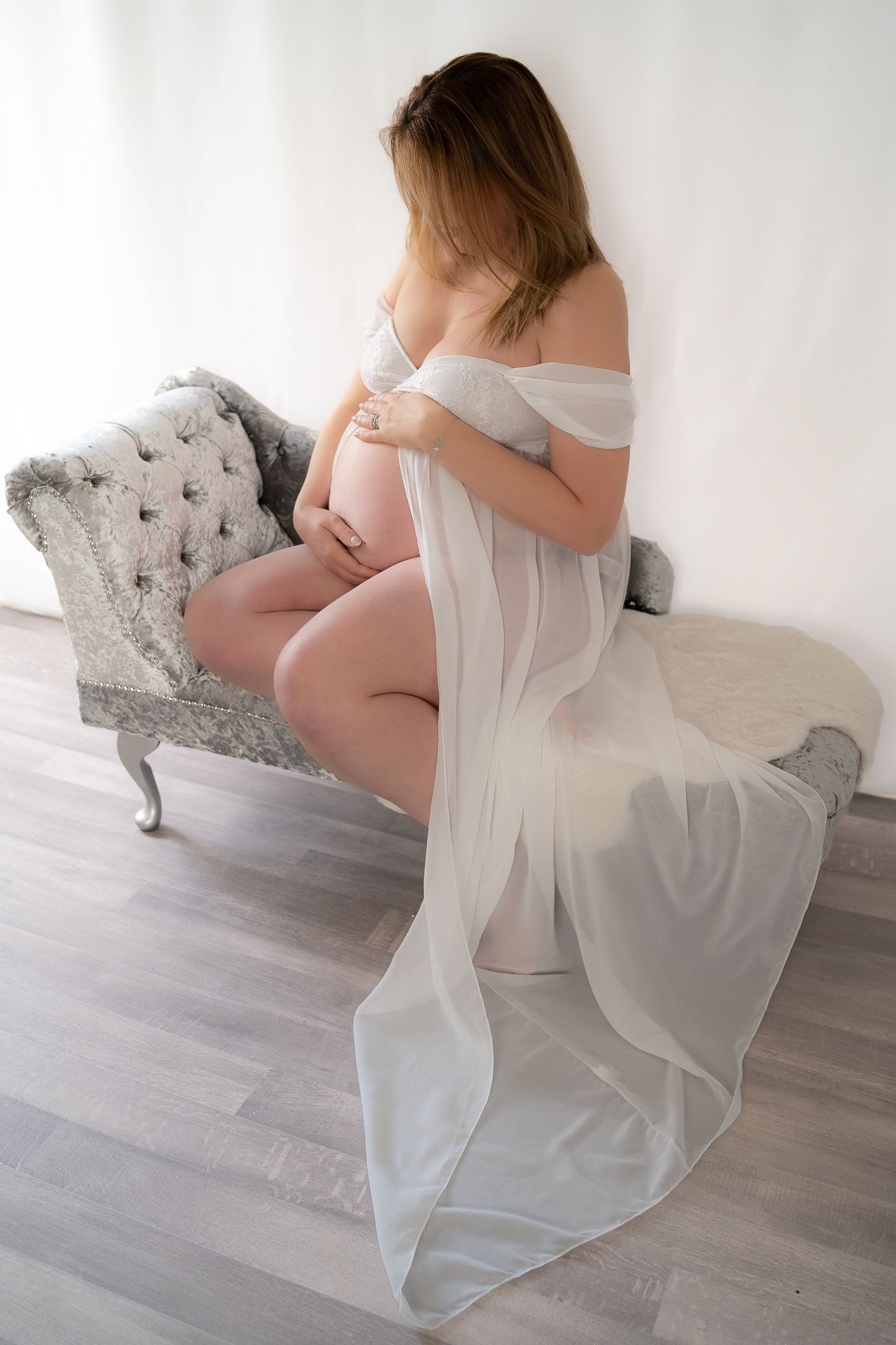 Maternity portrait with flowing white fabric on elegant grey chaise lounge.