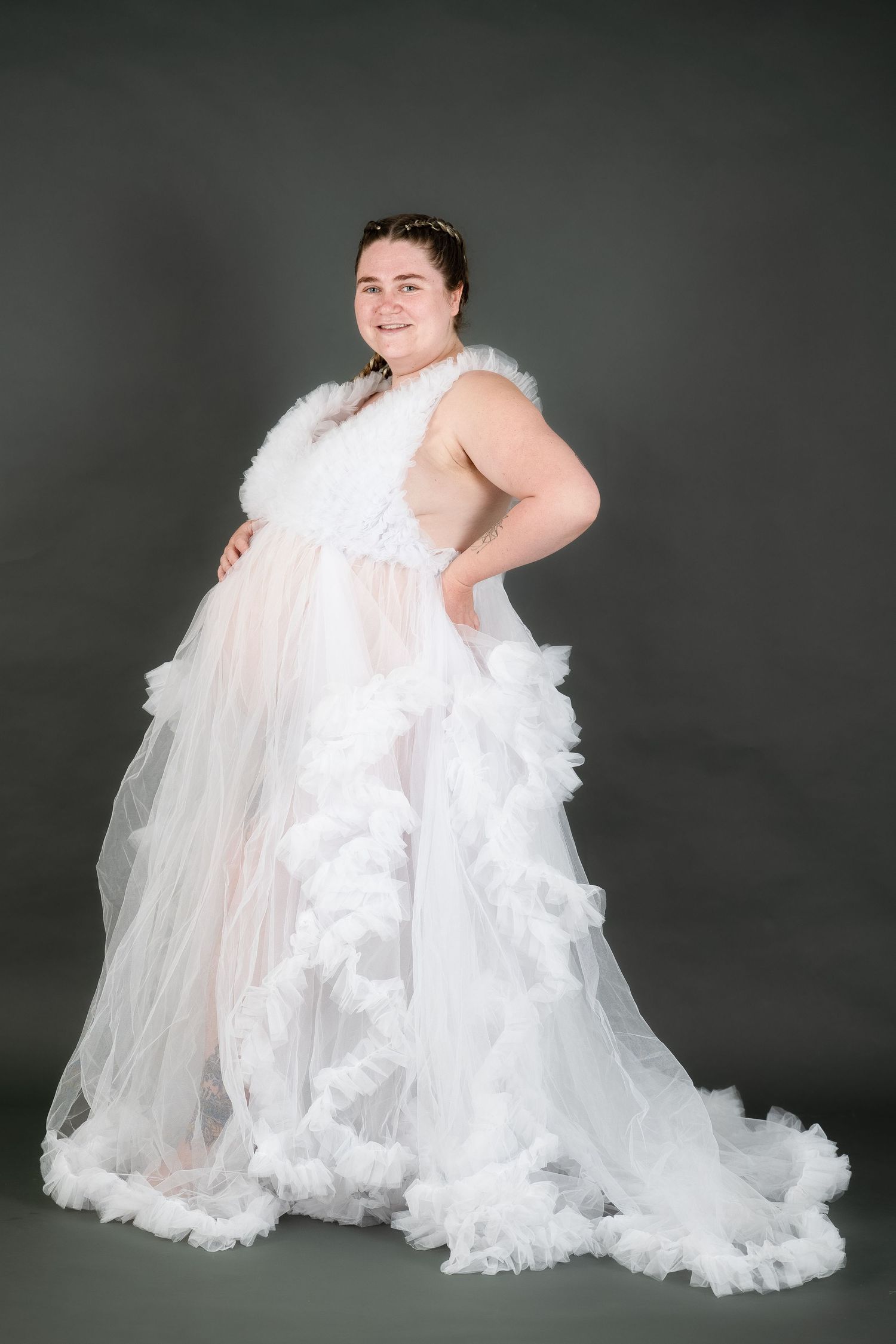 Dramatic maternity portrait in flowing white tulle gown against dark background.