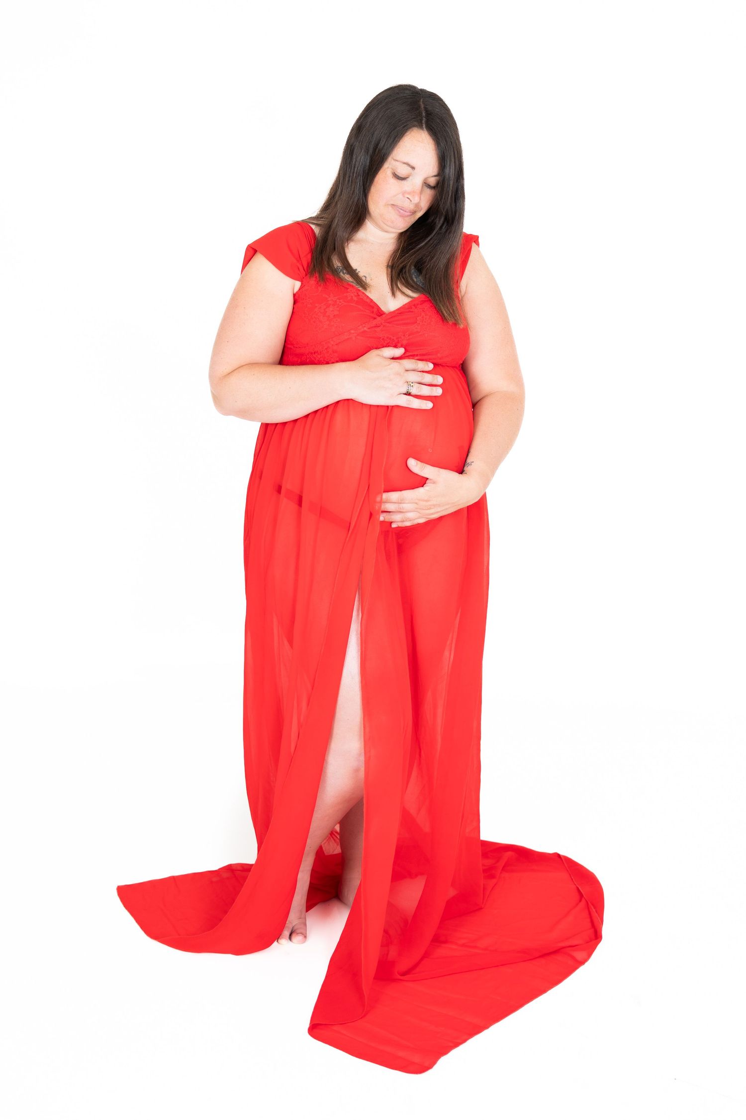 Expectant person in a flowing red dress poses against white background while cradling baby bump.