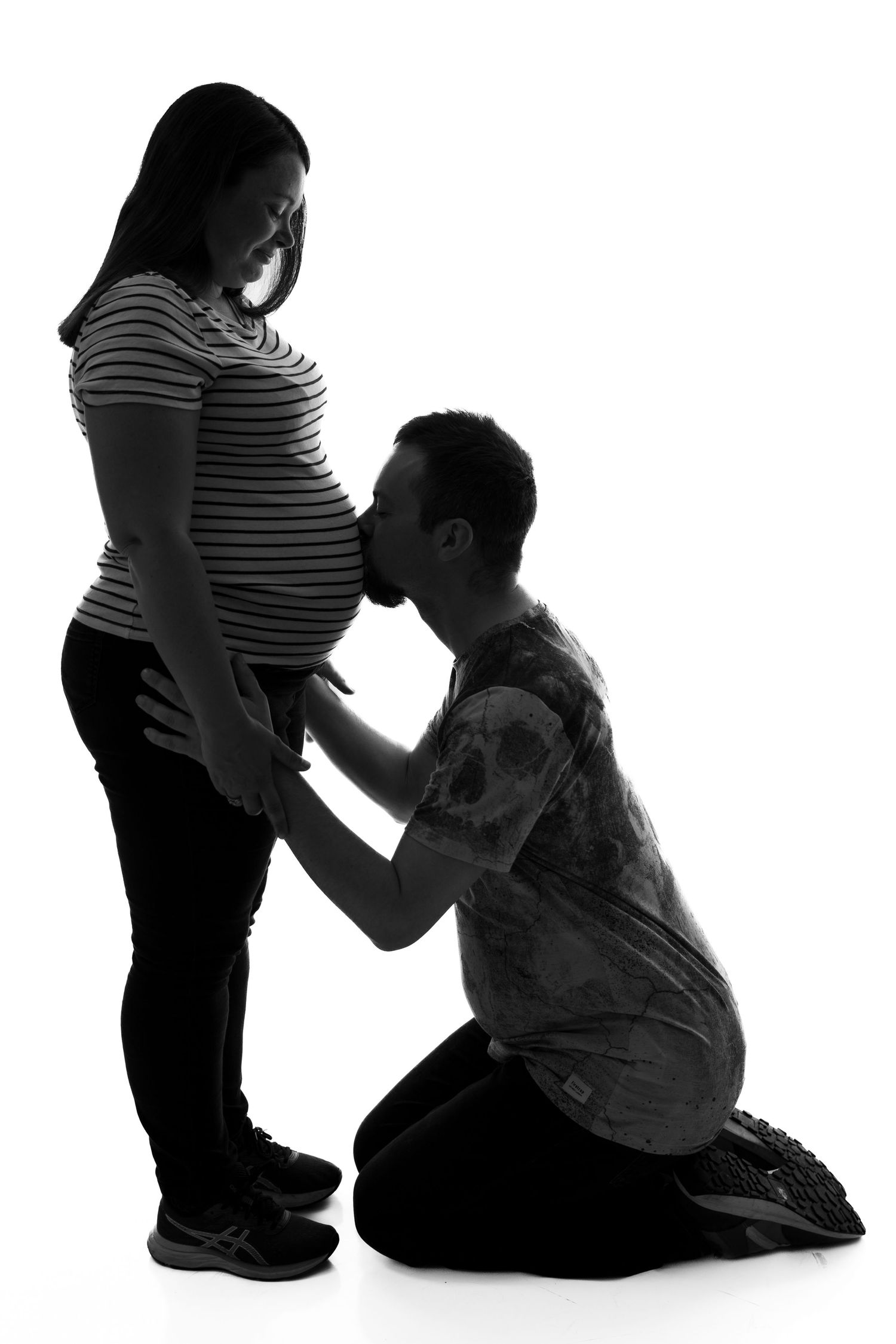 Black and white silhouette of an expectant couple sharing an intimate moment as the partner kneels beside the pregnant belly.