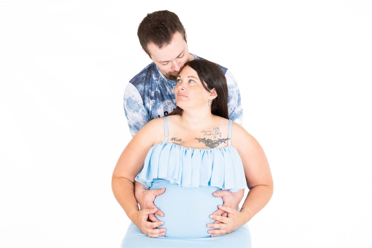 A couple wearing matching light blue outfits embrace each other during a romantic outdoor photo session.