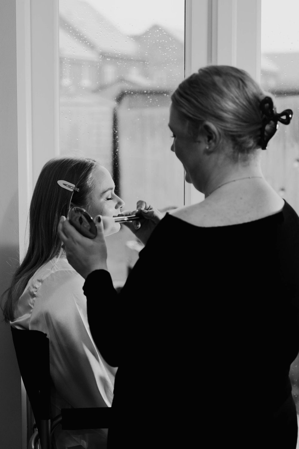 A makeup artist applies cosmetics to a client in a black and white photograph.