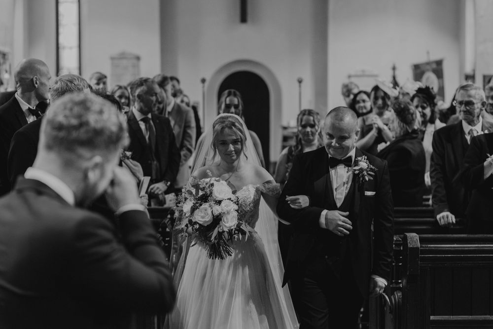 Church wedding ceremony with guests seated in wooden pews.