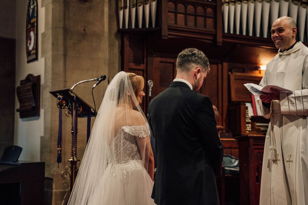 A wedding ceremony takes place in a church with elegant wooden pews and a decorated Christmas tree in the background.