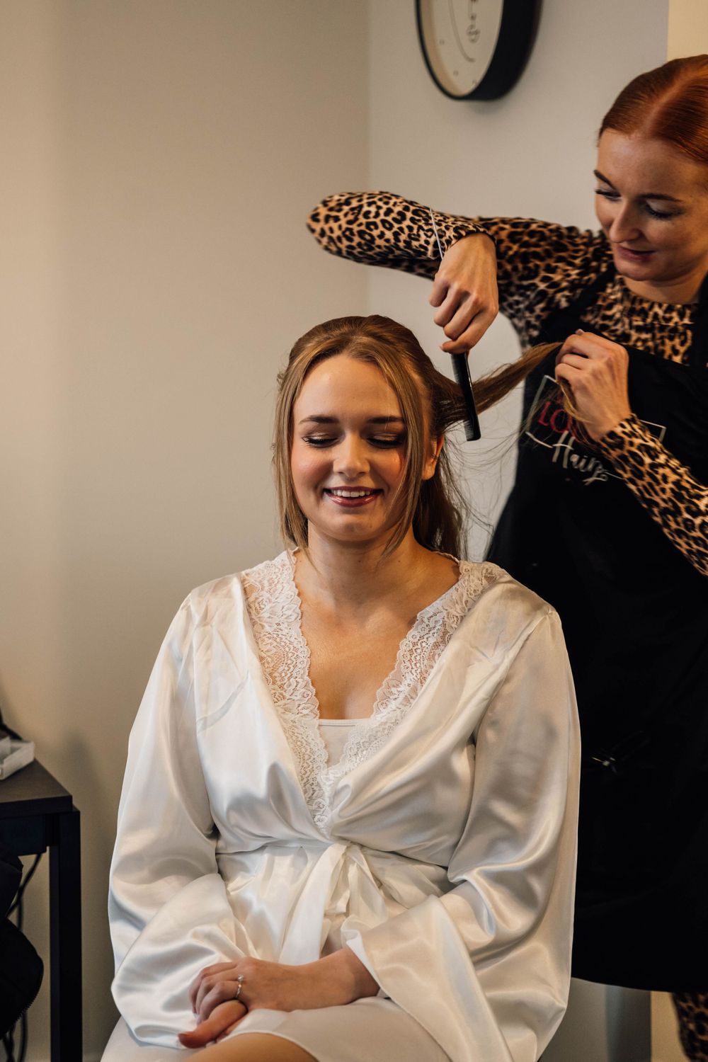 A hairstylist wearing a leopard print top styles a client's hair during wedding preparations.