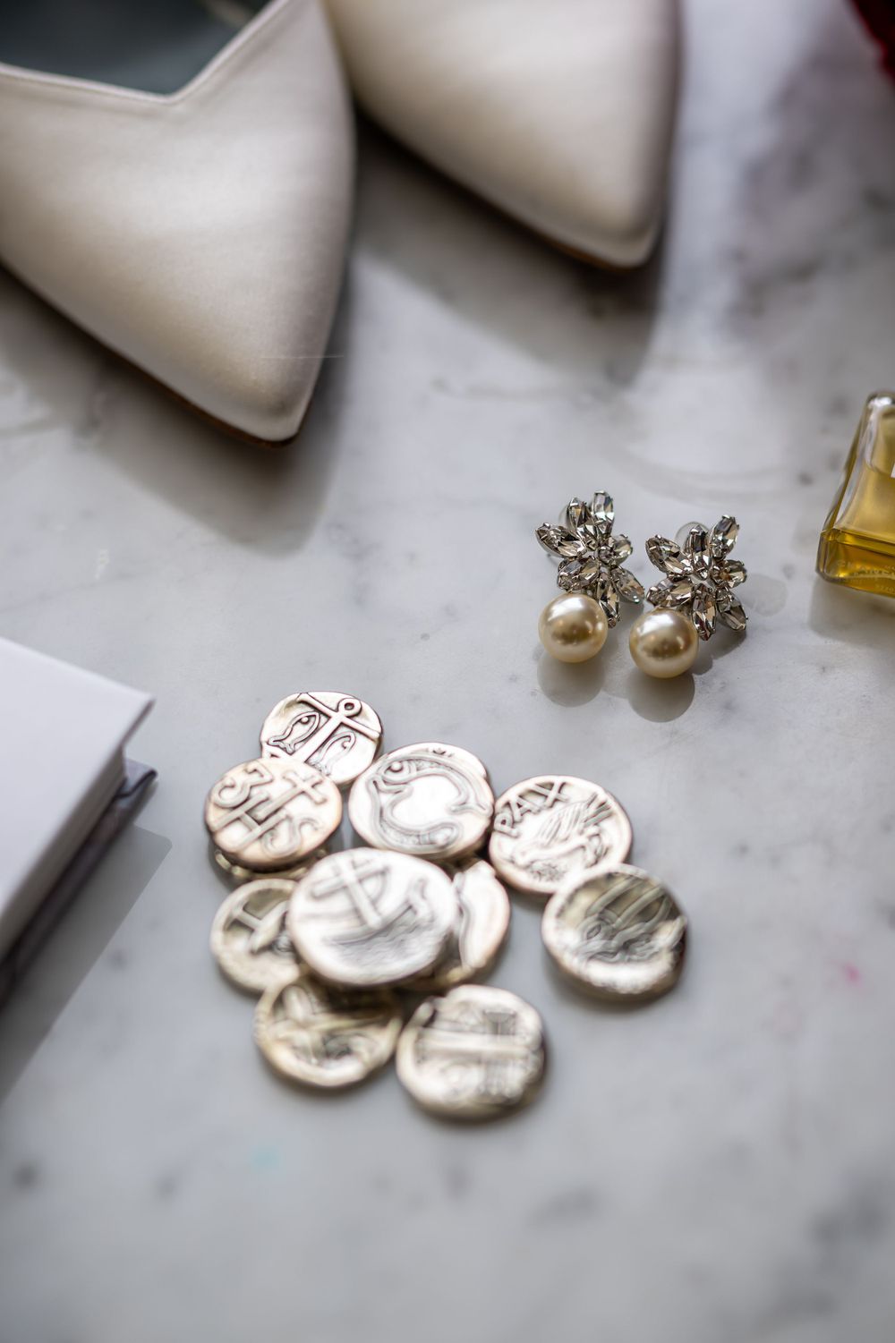 Pearl earrings and silver commemorative coins arranged on white marble surface.