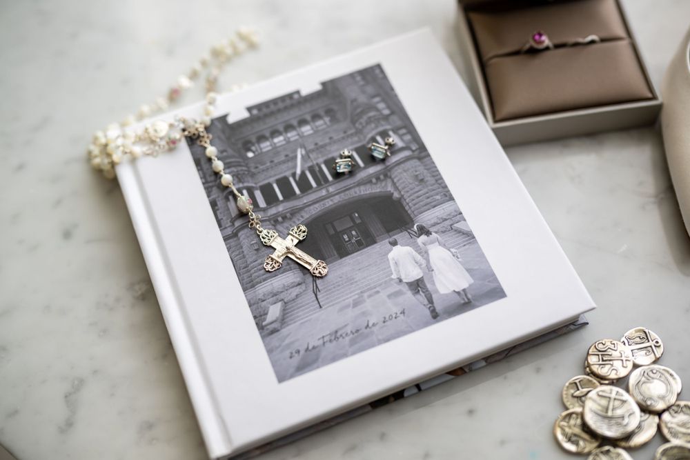 Wedding photo album and jewelry displayed on marble surface with ring box and delicate details.