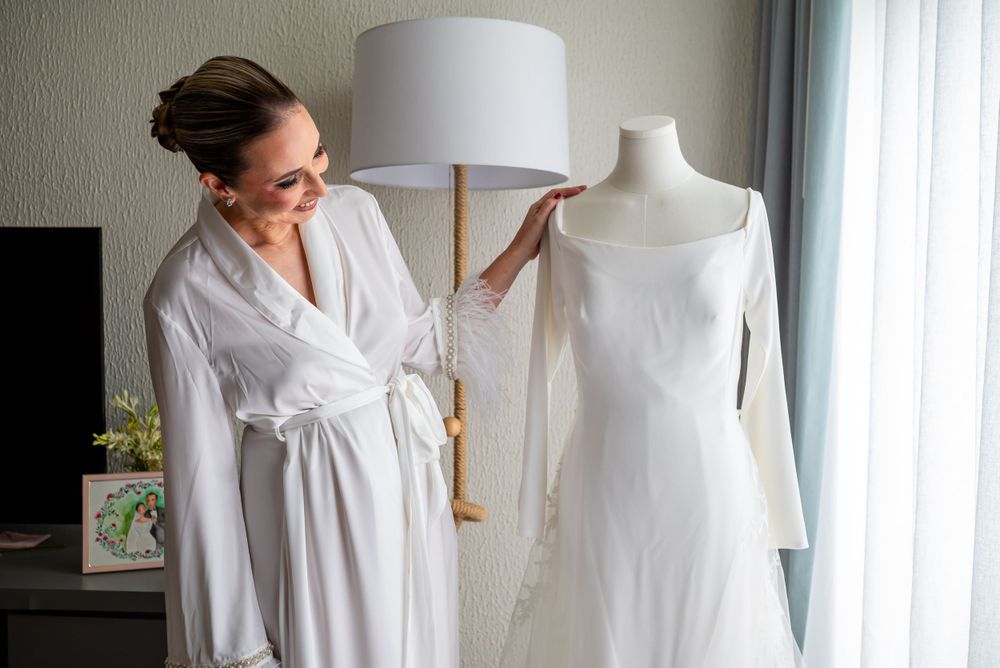 Wedding dress on mannequin with person in white robe examining details.
