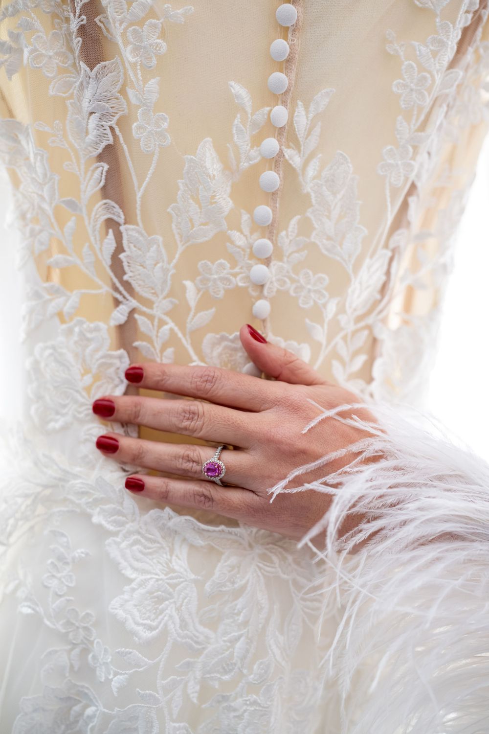 Close-up of manicured hands with rings against lace wedding dress detail.