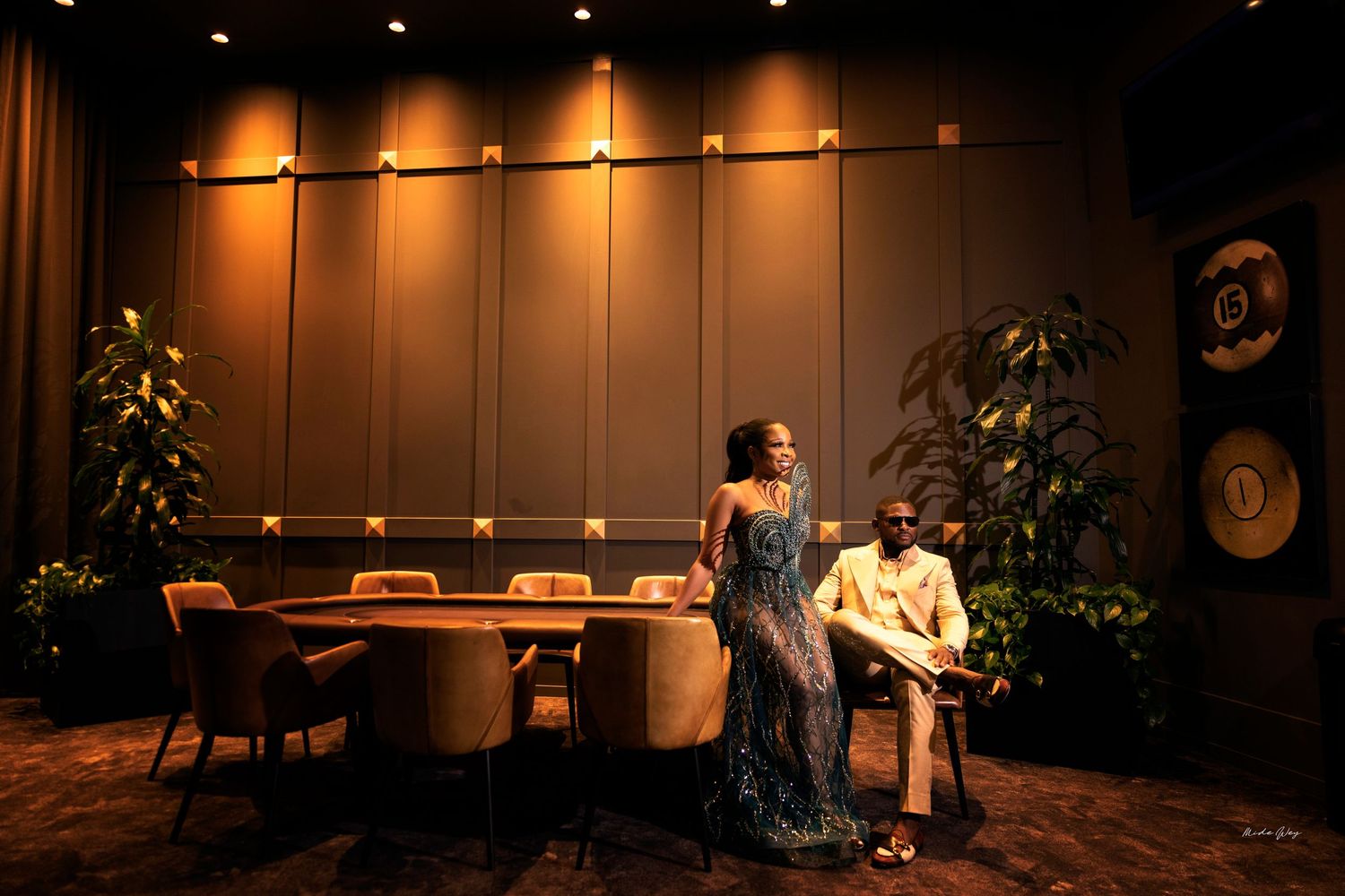 Couple poses in elegant evening attire within modern restaurant setting with mood lighting.