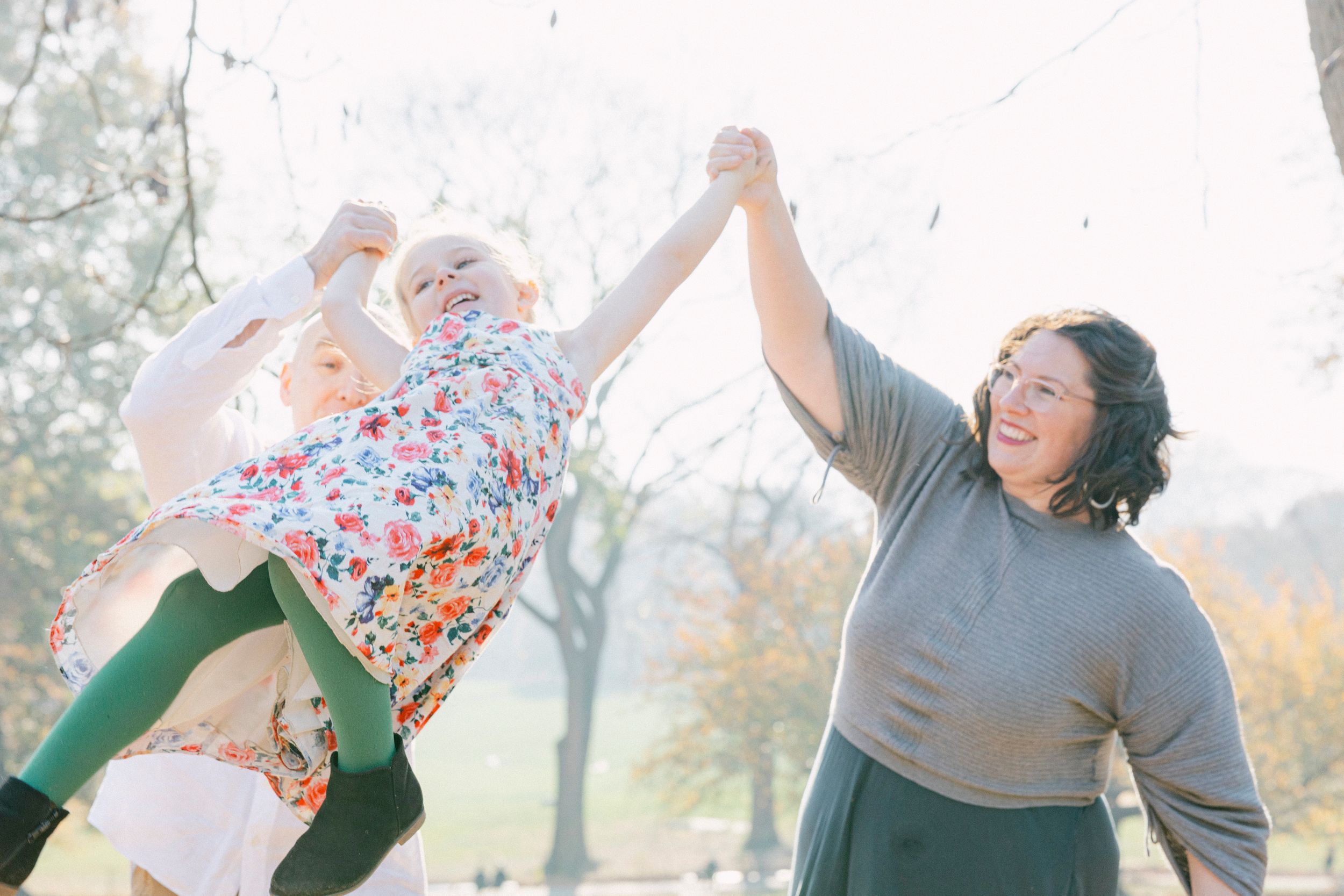 A family plays together outdoors, lifting and spinning in joyful movement.