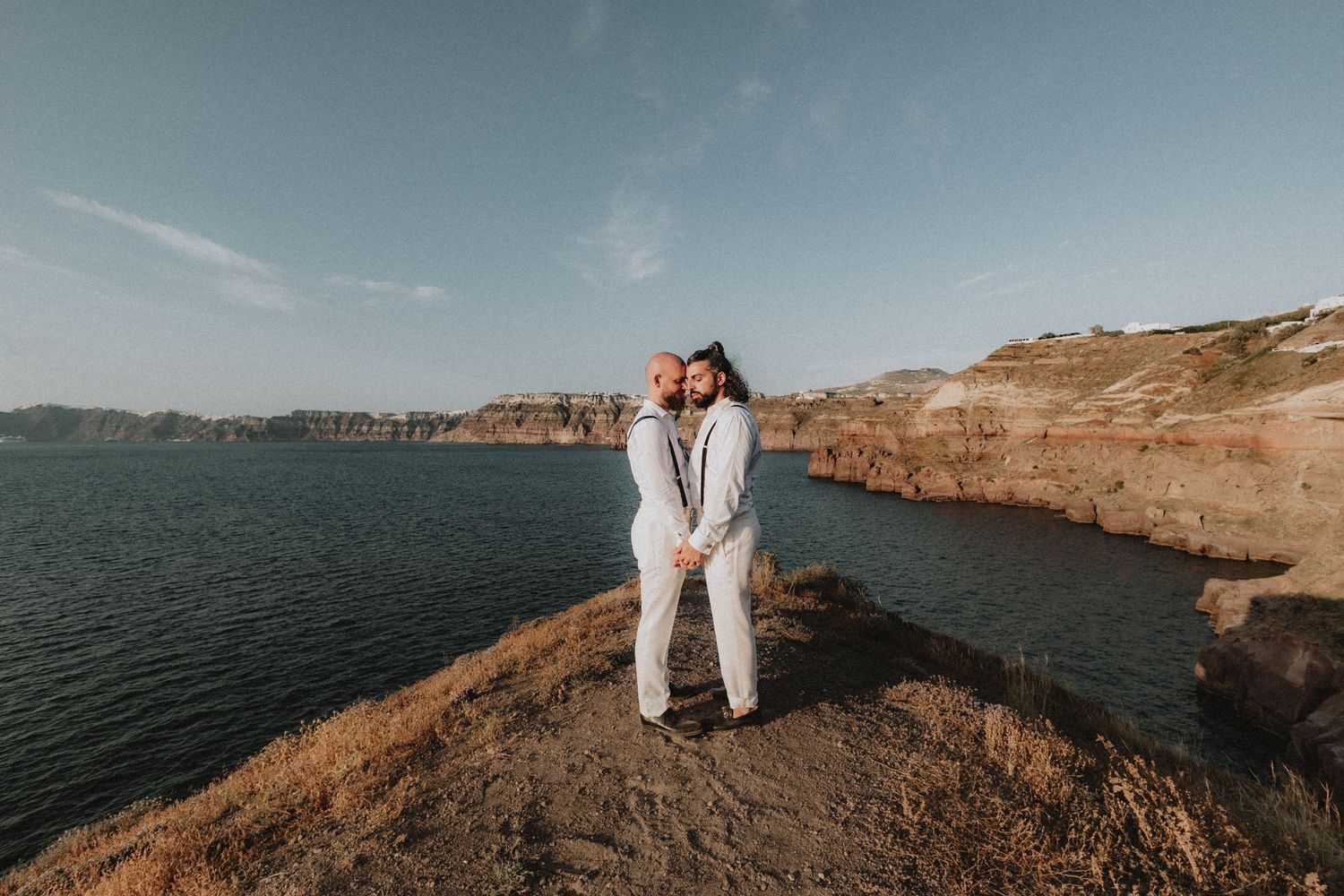 photo of a gay couple holding hands on the cliffs of Santorini islands in Greece during their wedding.