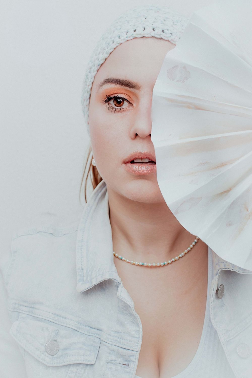 Artistic fashion portrait with white veil and pearl necklace against light background creating ethereal mood.
